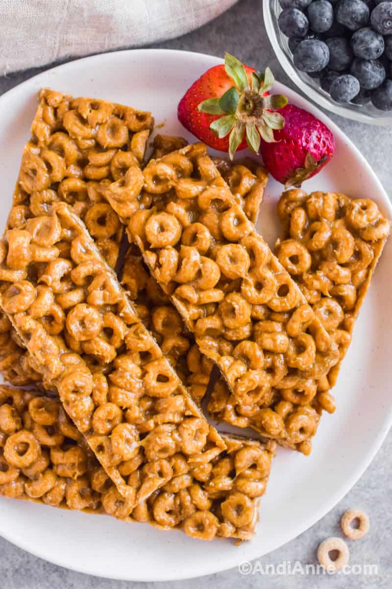 Cereal bars stacked on a plate with strawberries and blueberries.