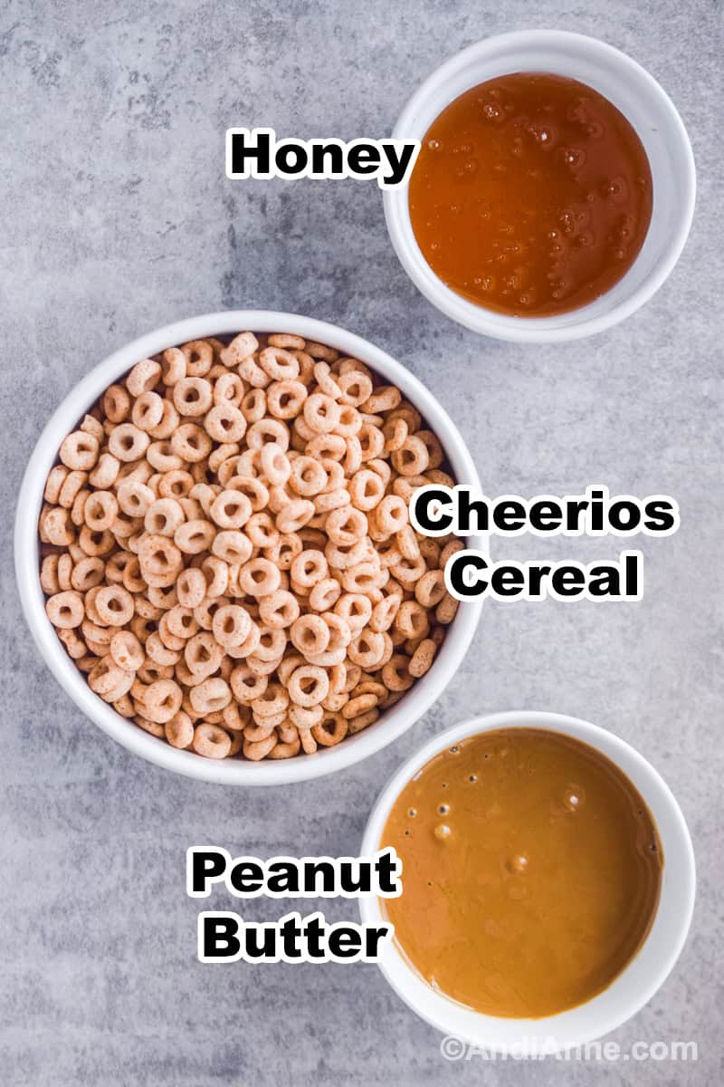 Ingredients to make recipe in bowls, including bowl of Cheerios cereal, bowl of peanut butter, and bowl of honey.