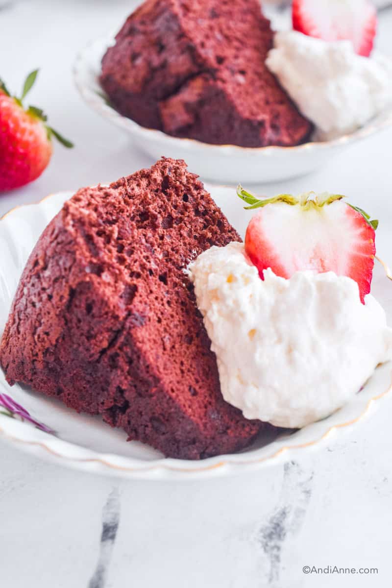A slice of chocolate angel food cake with a dollop of whipped cream and sliced strawberry. Another serving of cake and a strawberry are blurred in the background.