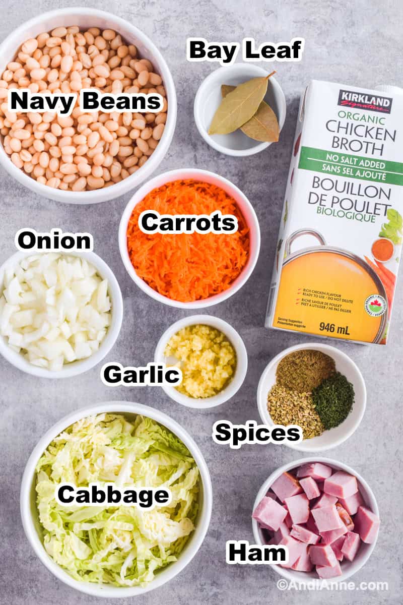 Ingredients to make soup on counter in bowls including white navy beans, chopped onion, sliced cabbage and carton of broth.