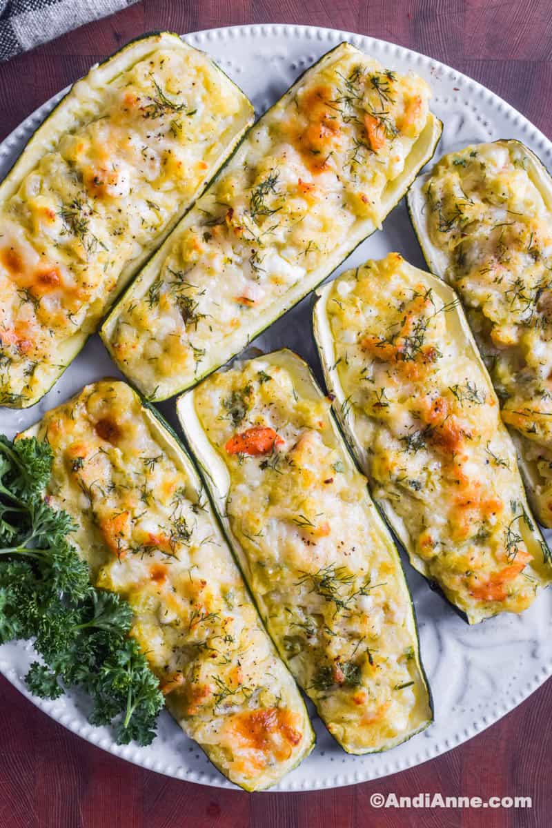 Slices of crab stuffed zucchini on a white plate with a bit of fresh parsley beside it.
