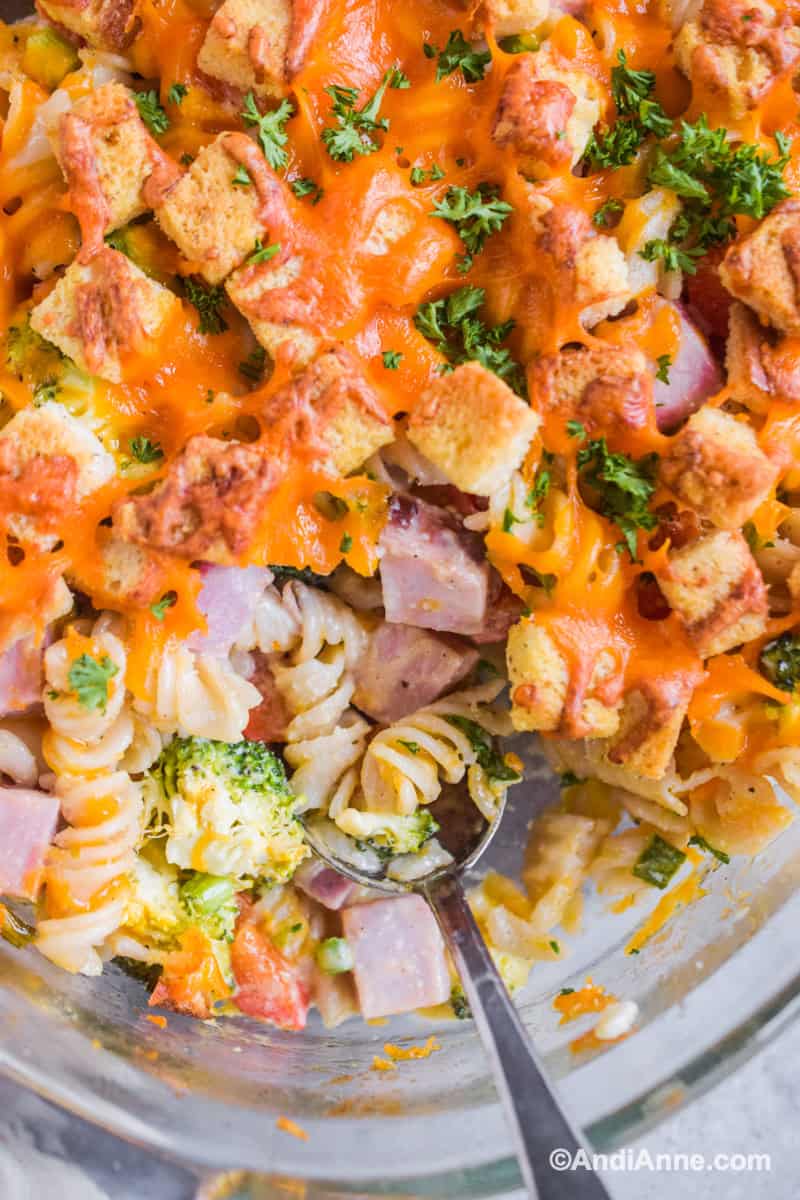 Close up of spoon digging into casserole with croutons, cheese and spiral pasta.