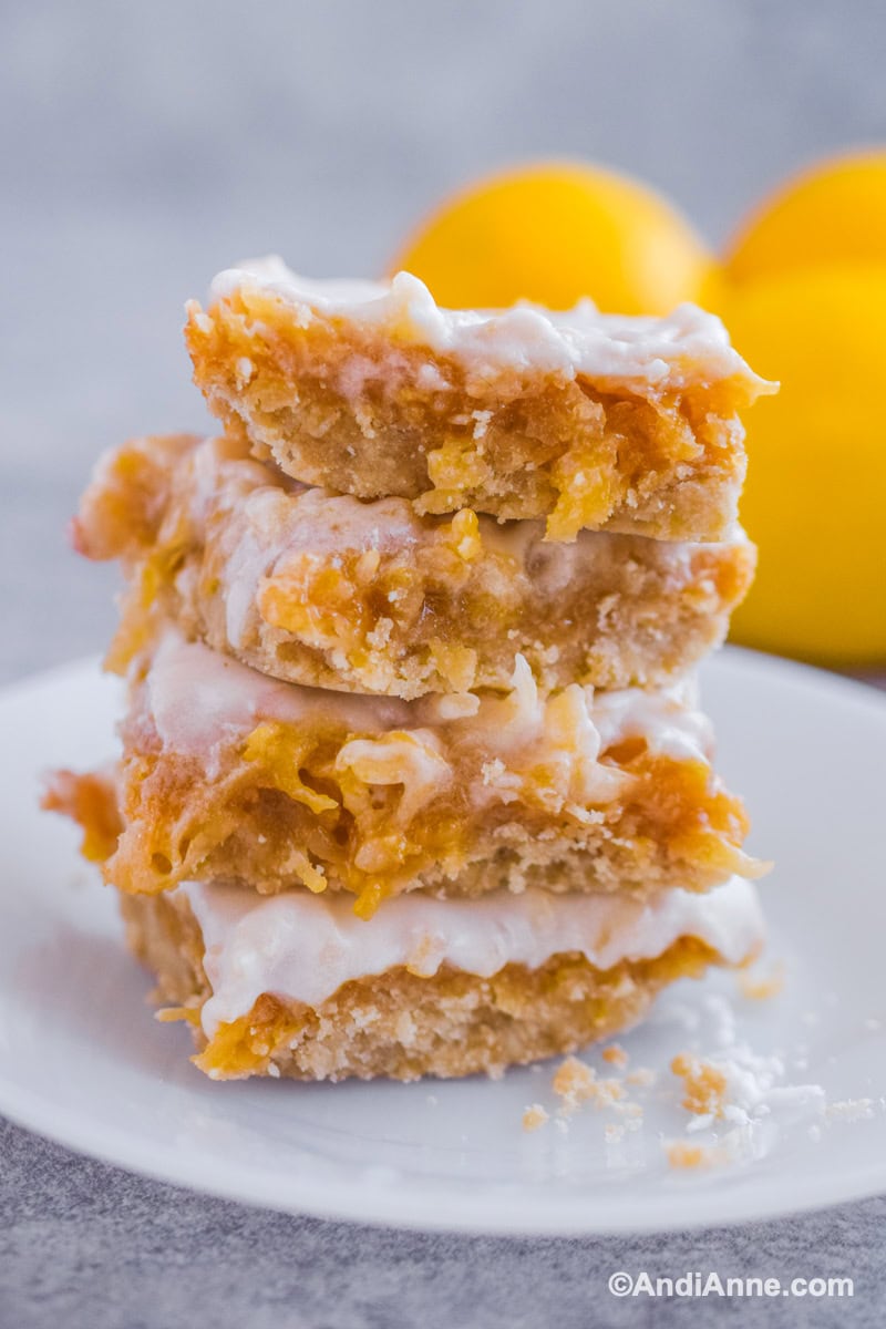 Four lemon coconut squares stacked on top of eachother on a white plate.