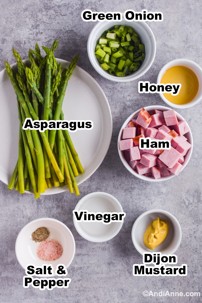 Ingredients to make recipe including asparagus, bowl of honey, chopped ham, bowl of vinegar, green onions, and dijon mustard.