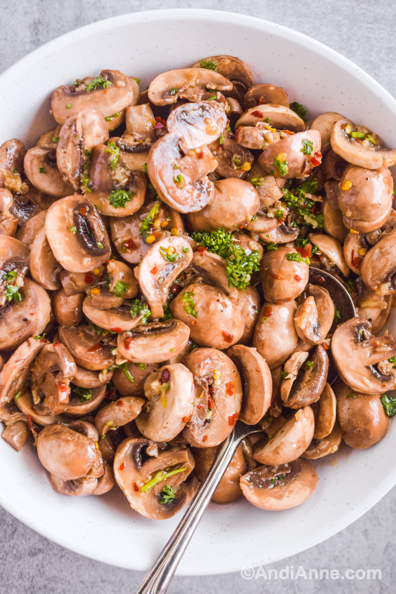 Marinated mushrooms in a white bowl with a spoon. Parsley sprinkled on top.