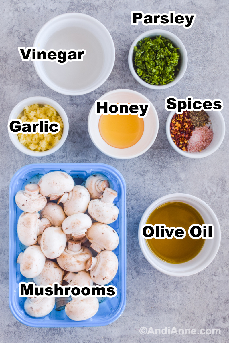 Recipe ingredients on counter including bowl of vinegar, chopped parsley, honey, minced garlic, olive oil and carton of white mushrooms.