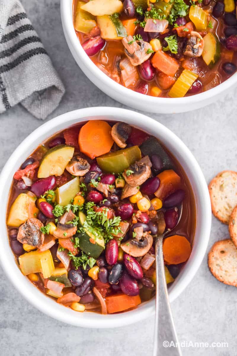 Looking down at white bowl with vegetarian chili with spoon and crackers beside it.