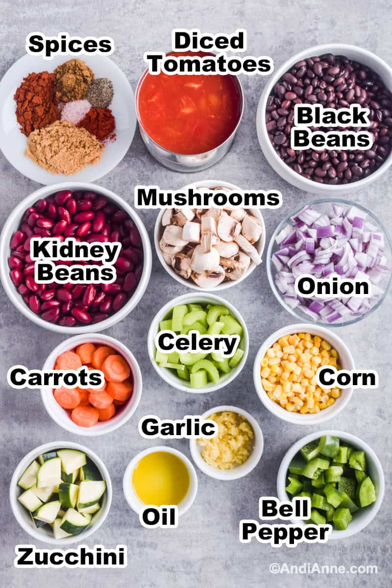 Ingredient to make the chili in bowls on counter including beans, mushrooms, carrots, celery, a can of diced tomatoes and a plate with all the spices used.