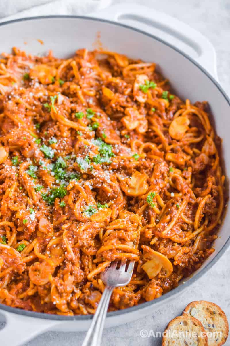 One pot spaghetti pasta with a fork in a white dutch oven. Parmesan and parsley sprinkled on top.