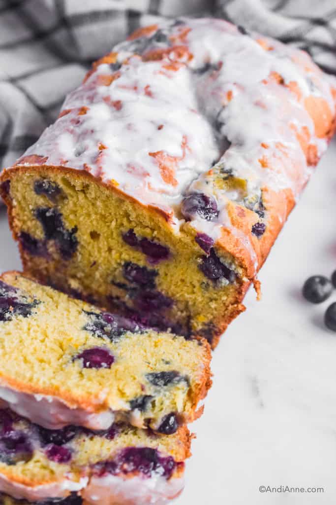 Orange blueberry pound cake with powdered sugar glaze and two slices cut out of it.