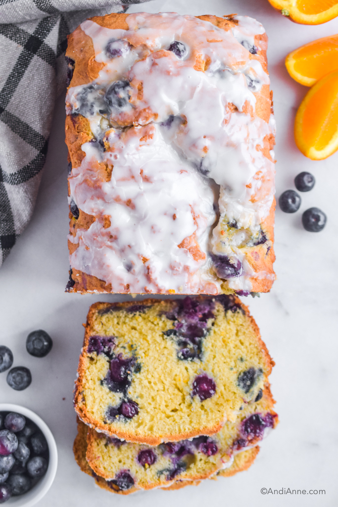 Looking down at pound cake with three slices cut out, fresh blueberries sprinkled around it and slices of orange.