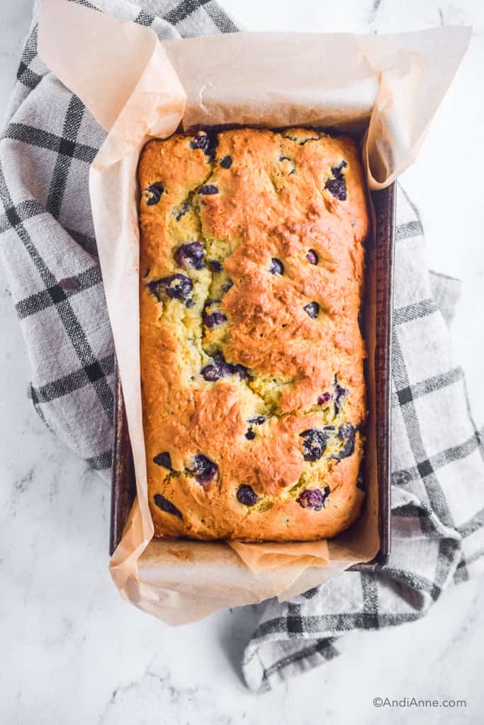 Bake pound cake in large loaf pan lined with parchment paper on top of a black and white plaid kitchen towel.