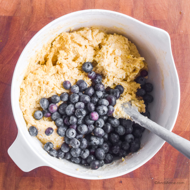 Batter with blueberries in white bowl with spatula.