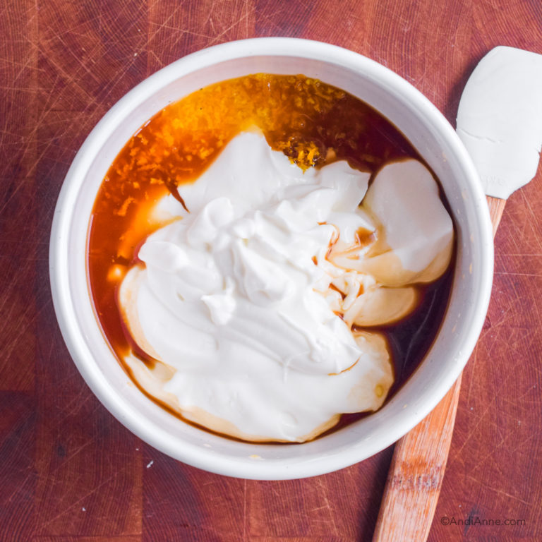 Bowl with yogurt, vanilla extract, zest and orange juice. Small spatula beside bowl.