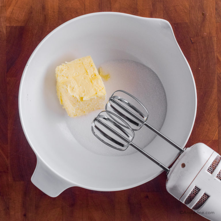 butter and sugar in a white bowl with hand mixer beside.