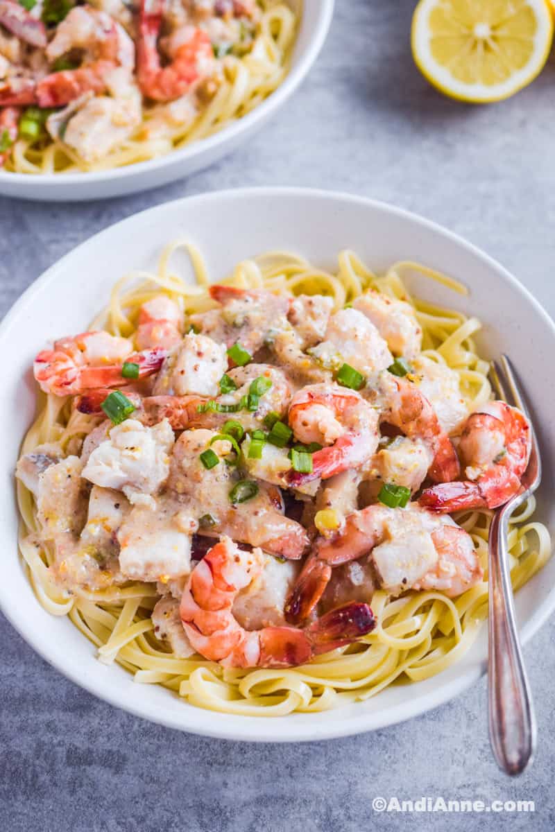 Pasta with shrimp and cod with chopped green onions in a white bowl with a fork.