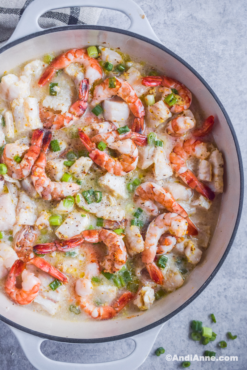 Shrimp, cod, chopped onions and a buttery sauce in a large white pot.