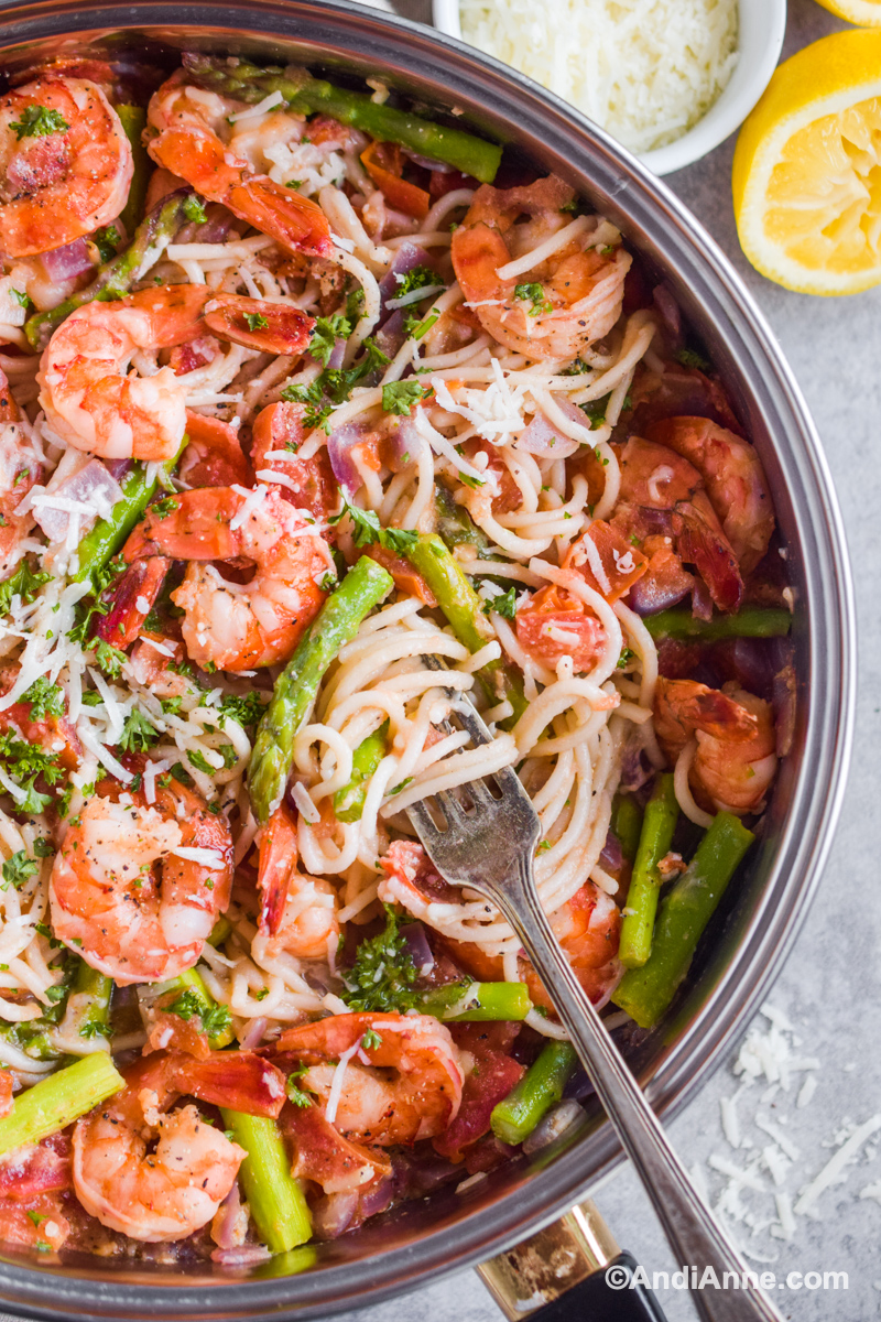 Close up of recipe in pot, a fork twists noodles beside cooked shrimp and chopped asparagus.