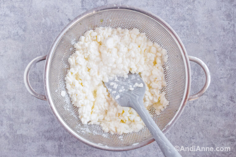 Cottage cheese in a strainer with a spatula.