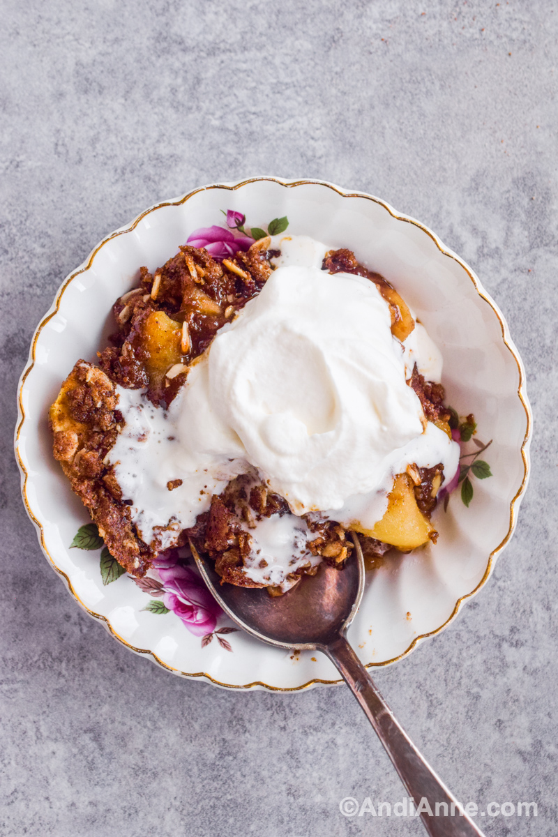 White dish with crumble, whipped cream and spoon inside.