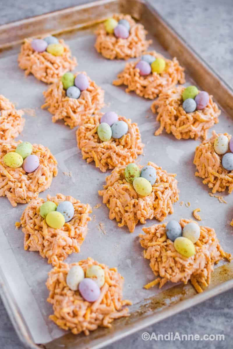 Side angle looking at birds nest cookies with chow mein noodles arranged in rows on a baking sheet.