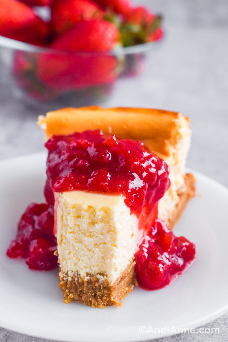 A slice of cheesecake with strawberry sauce drizzled over top and piece cut out of the front. 