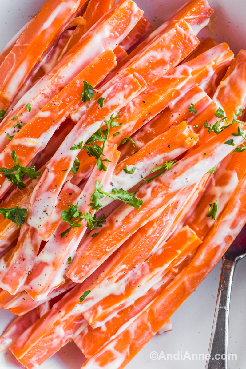 Close up of sliced carrots with creamy sauce and chopped parsley.