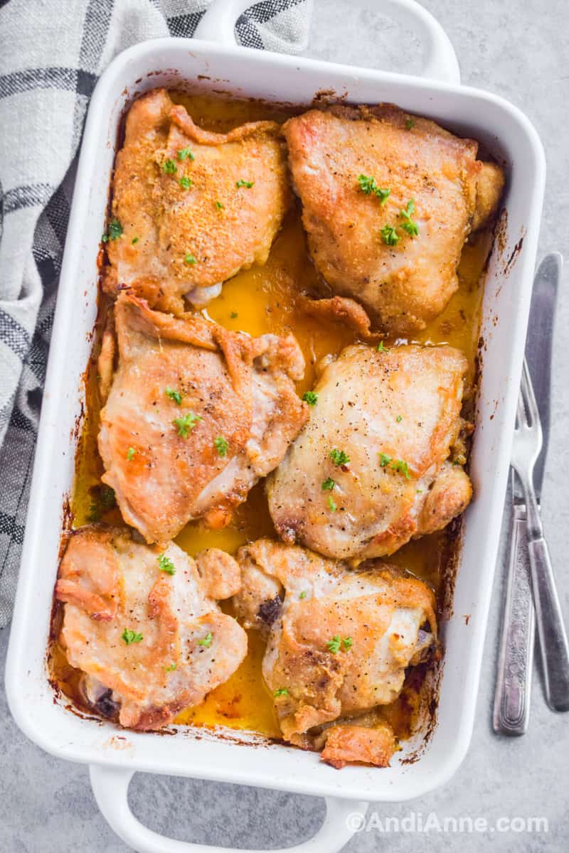 Looking down at white casserole dish with six oven fried chicken thighs.