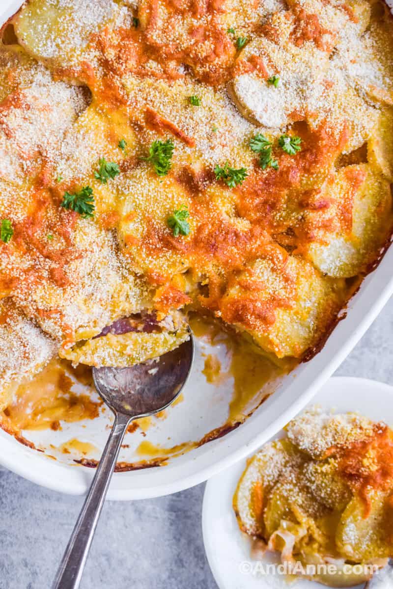 Slice of recipe on a white plate beside full casserole dish with potatoes and a spoon inside.