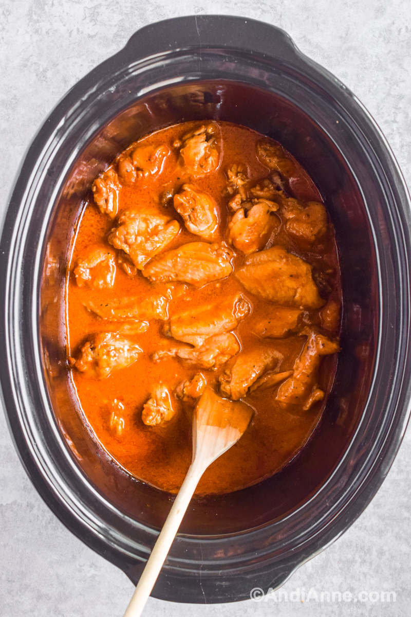 Slow cooker barbecue chicken wings in sauce with a spatula inside the pot.
