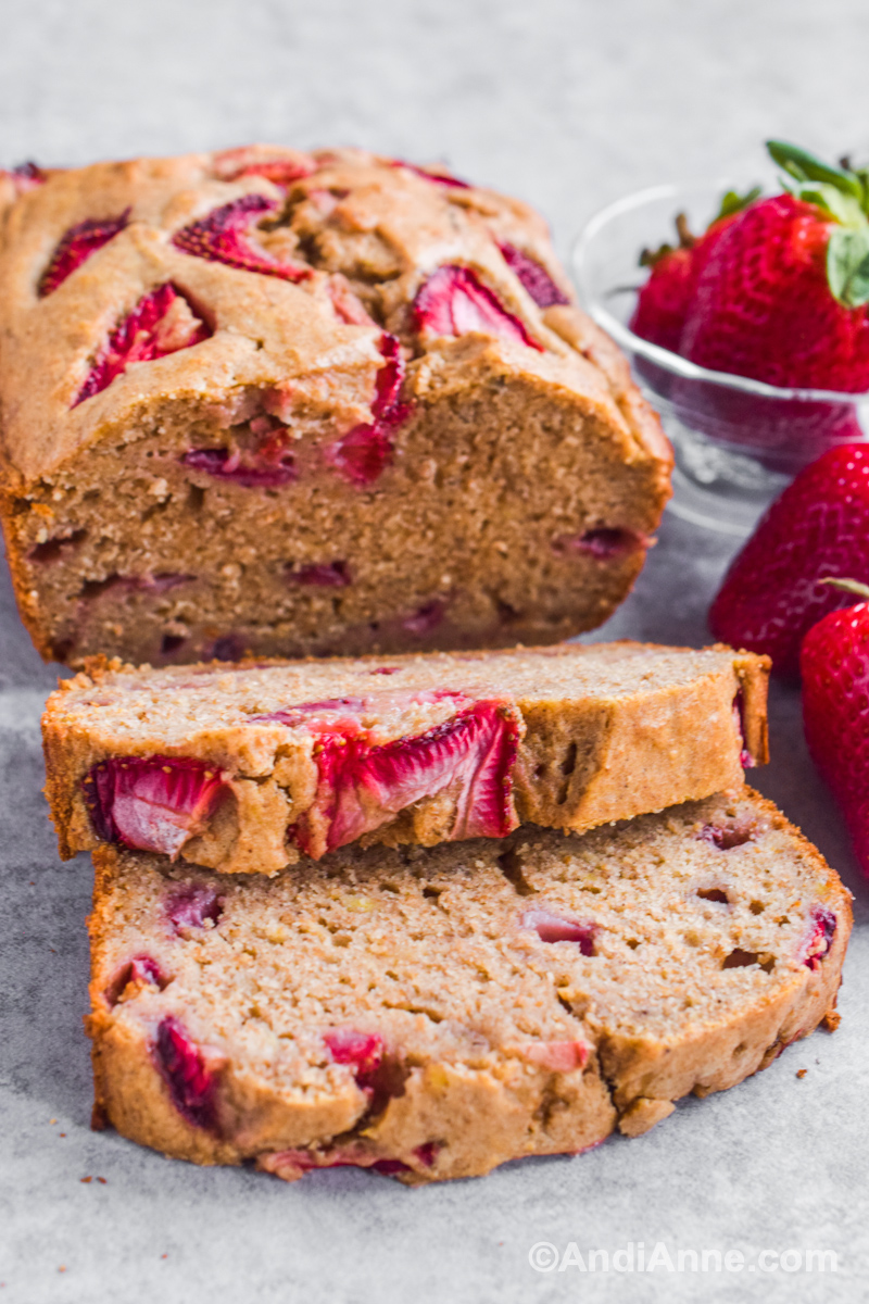 Strawberry banana bread loaf with slices cut out. Fresh strawberries beside it.