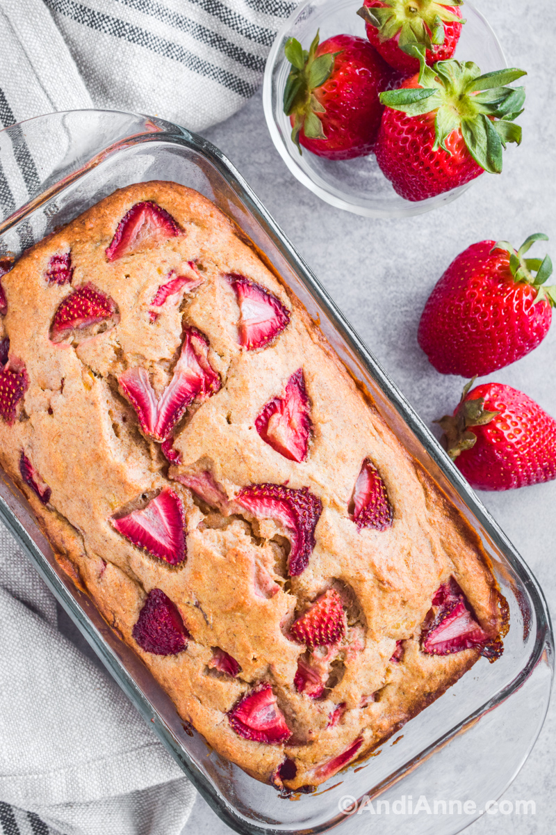 Close up of strawberry banana bread in glass loaf pan with fresh strawberries surrounding it.
