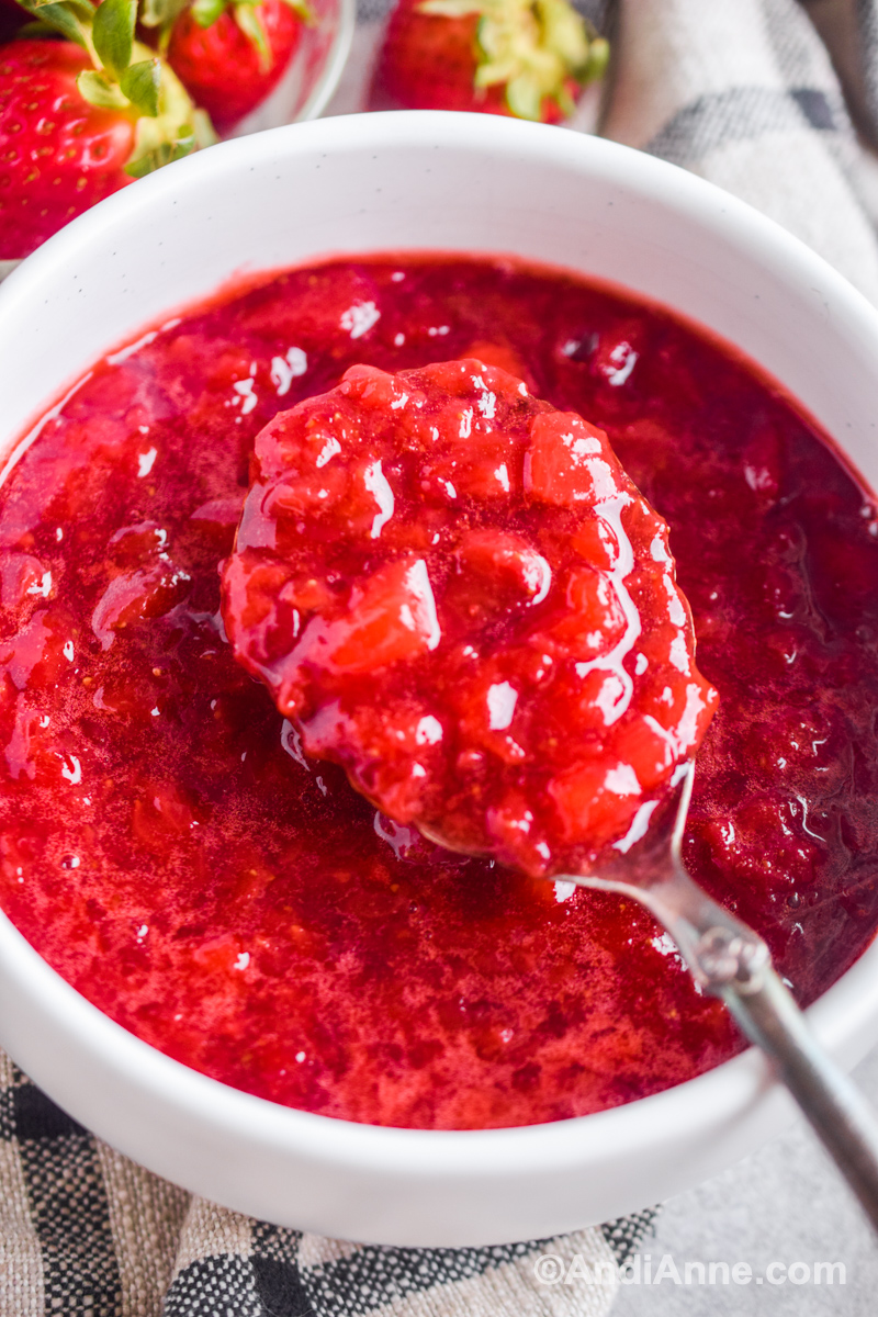 Strawberry sauce in a white bowl with a large spoon scooping some out.