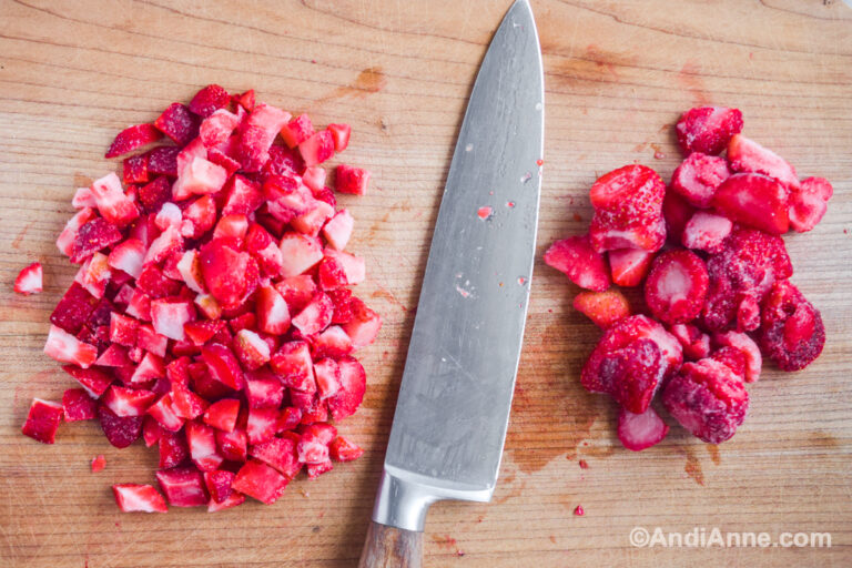 Chopped frozen strawberries on a cutting board with a knife.