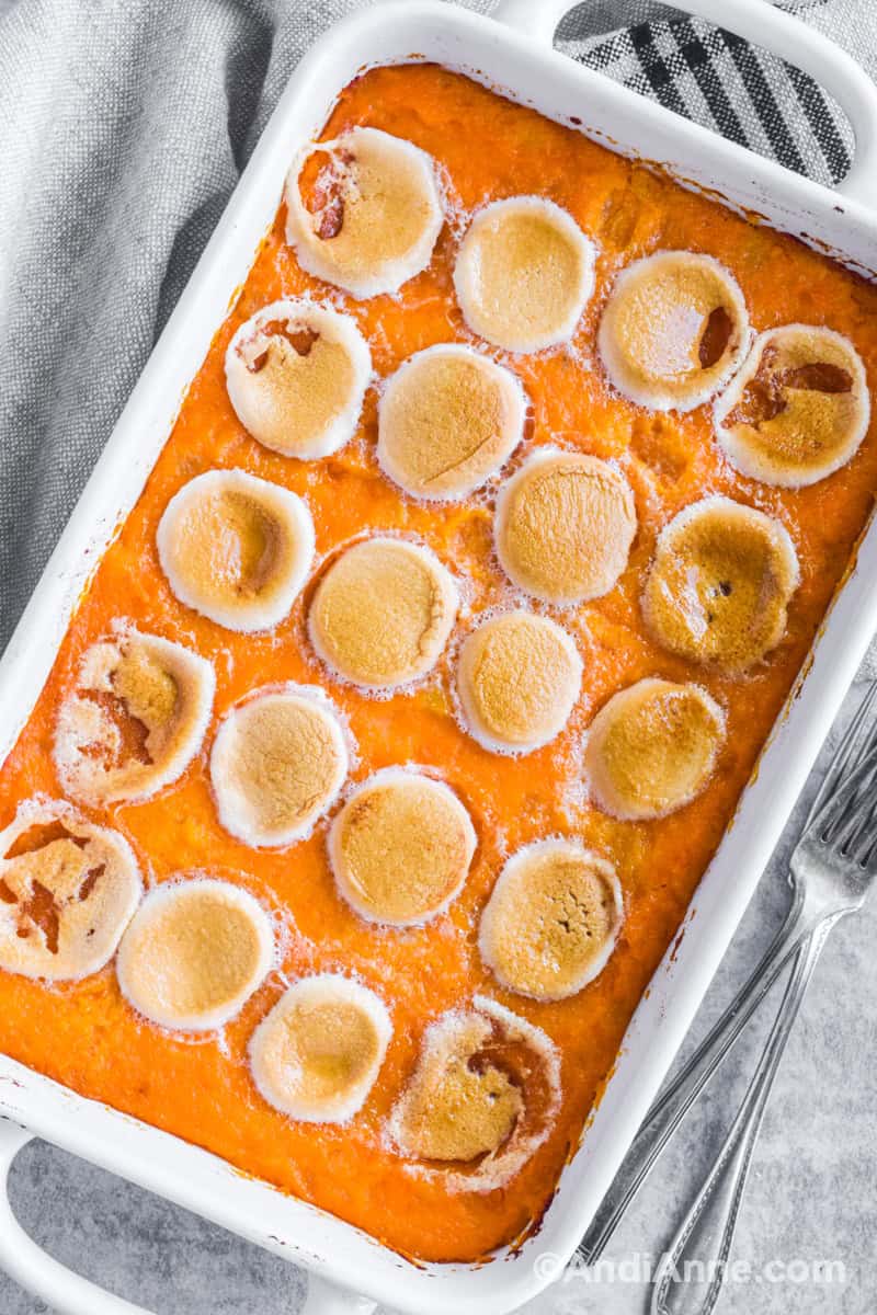 Sweet potato pineapple casserole with marshmallows with kitchen towel and forks beside.