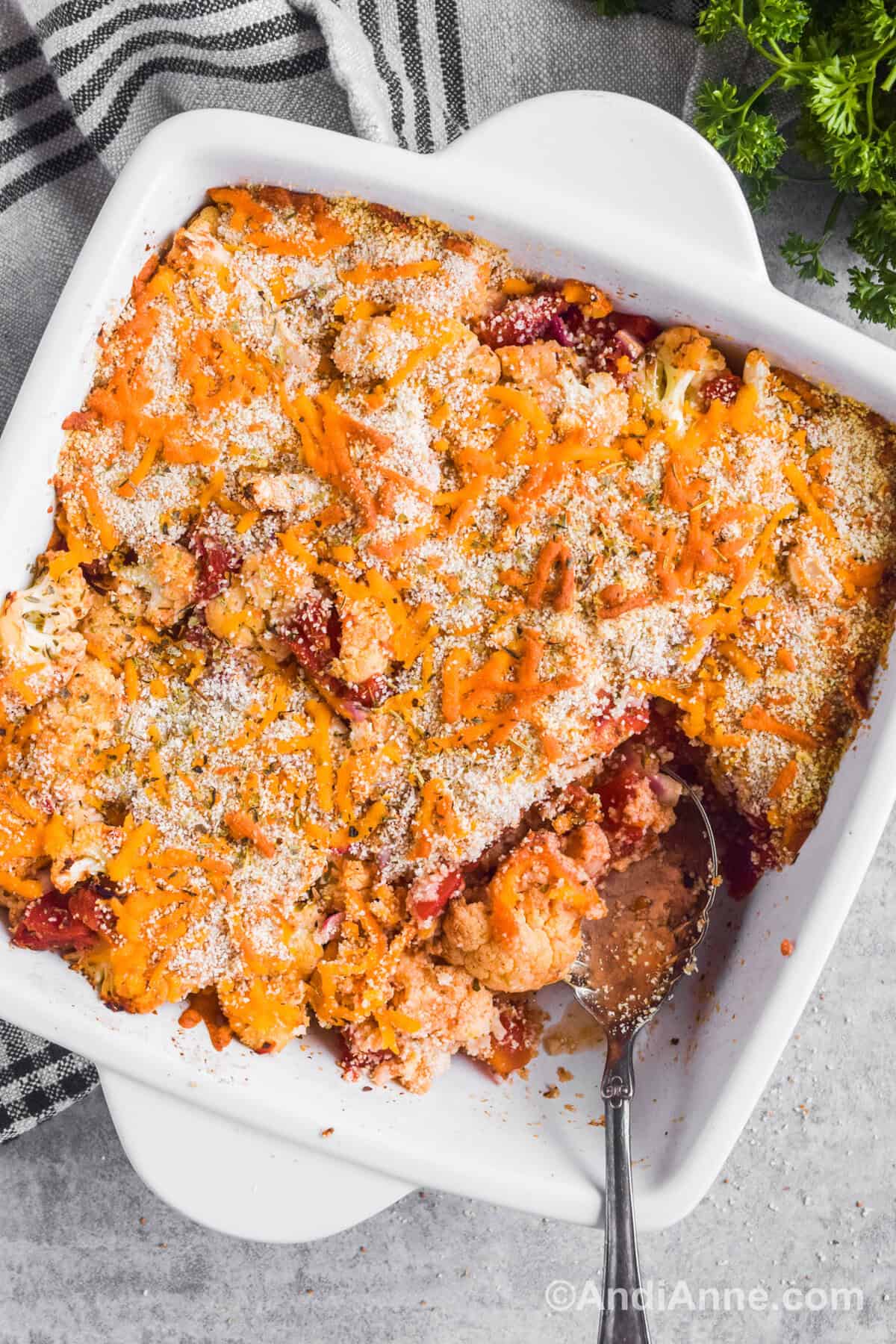 Baked cauliflower casserole recipe in a white square dish with a spoon in the bottom corner.
