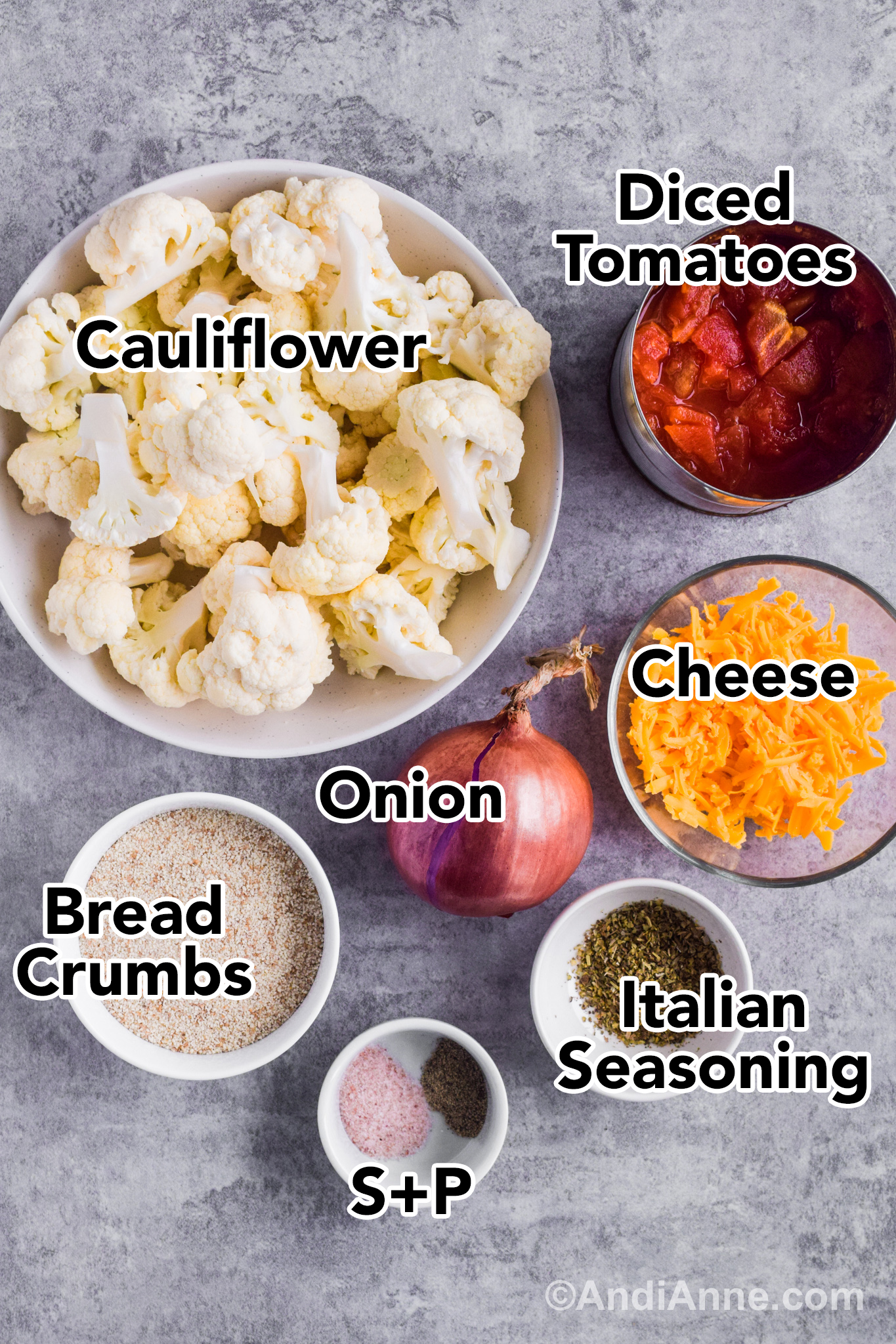 Recipe ingredients on the counter including a bowl of chopped cauliflower, canned diced tomatoes, shredded cheese, onion, breadcrumbs and herbs.