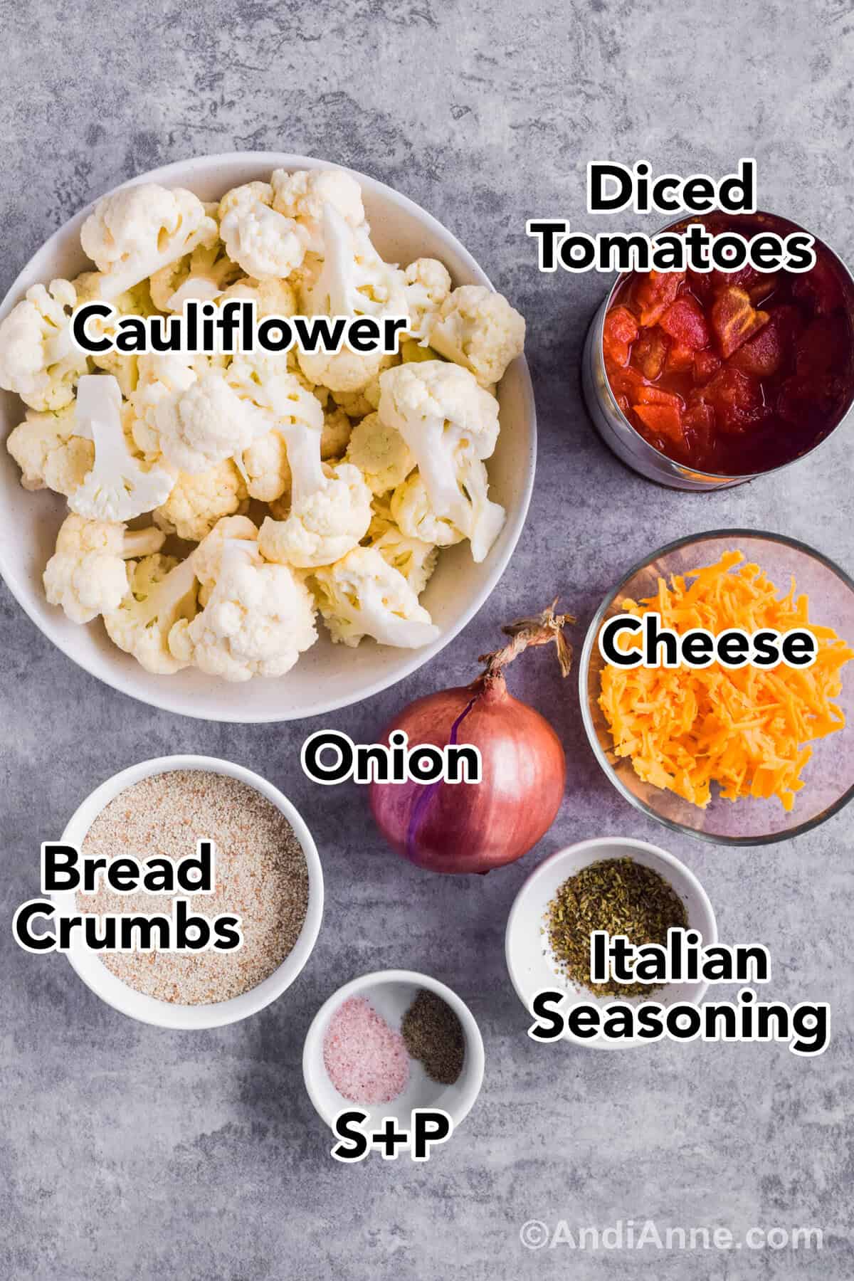 Recipe ingredients on the counter including a bowl of chopped cauliflower, canned diced tomatoes, shredded cheese, onion, breadcrumbs and herbs.