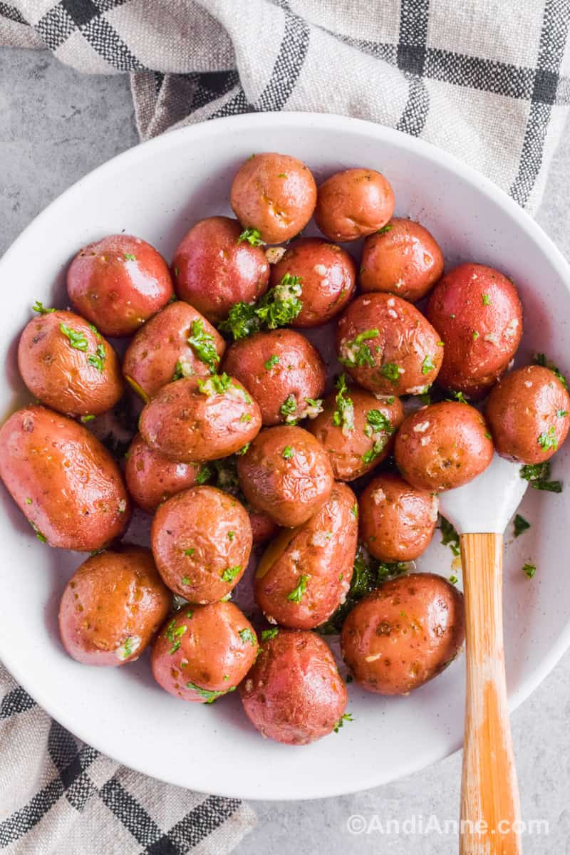 White bowl with microwaved baby red potatoes with garlic, parsley, oil and a small spatula.