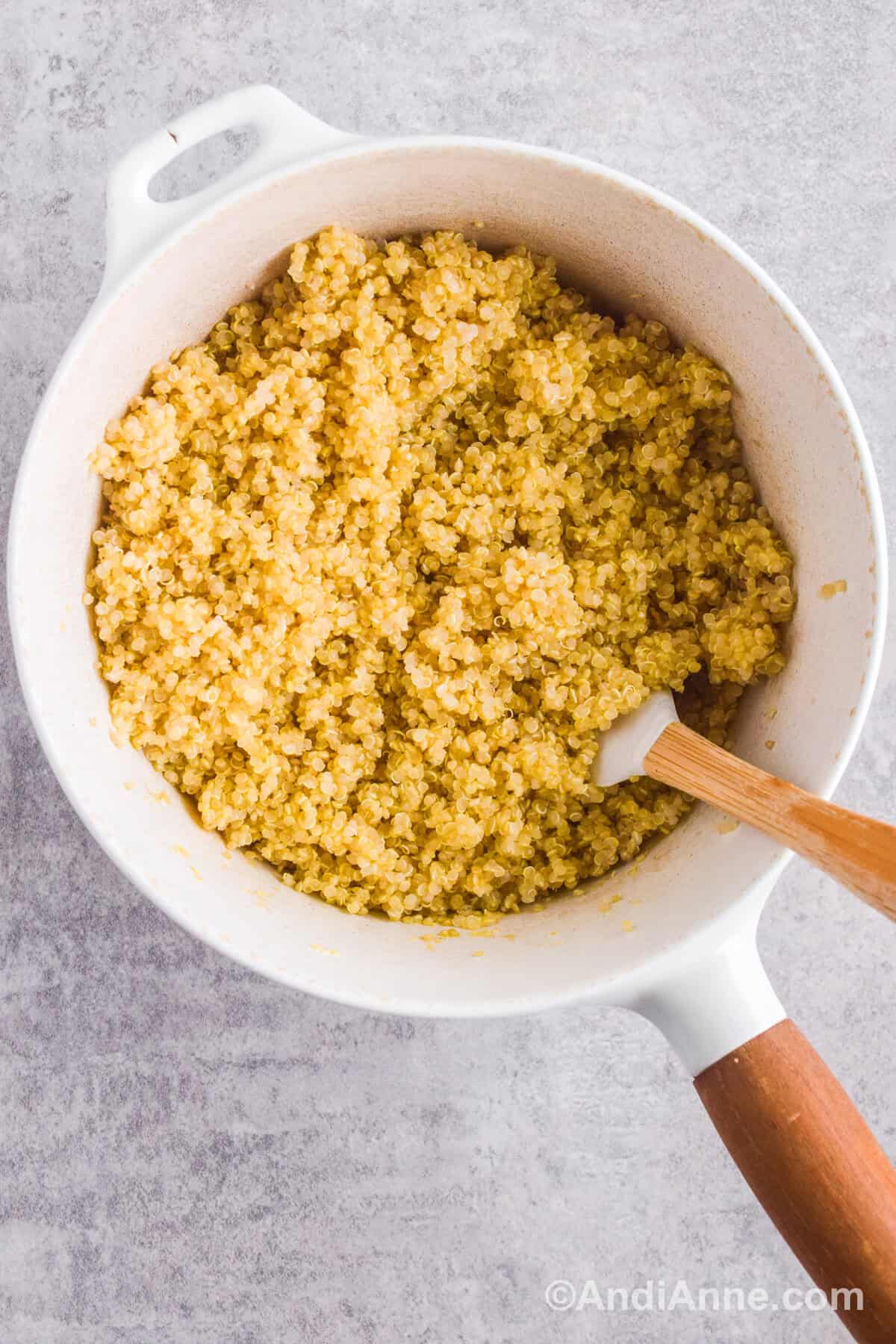 A white pot with cooked quinoa inside and a small spatula.