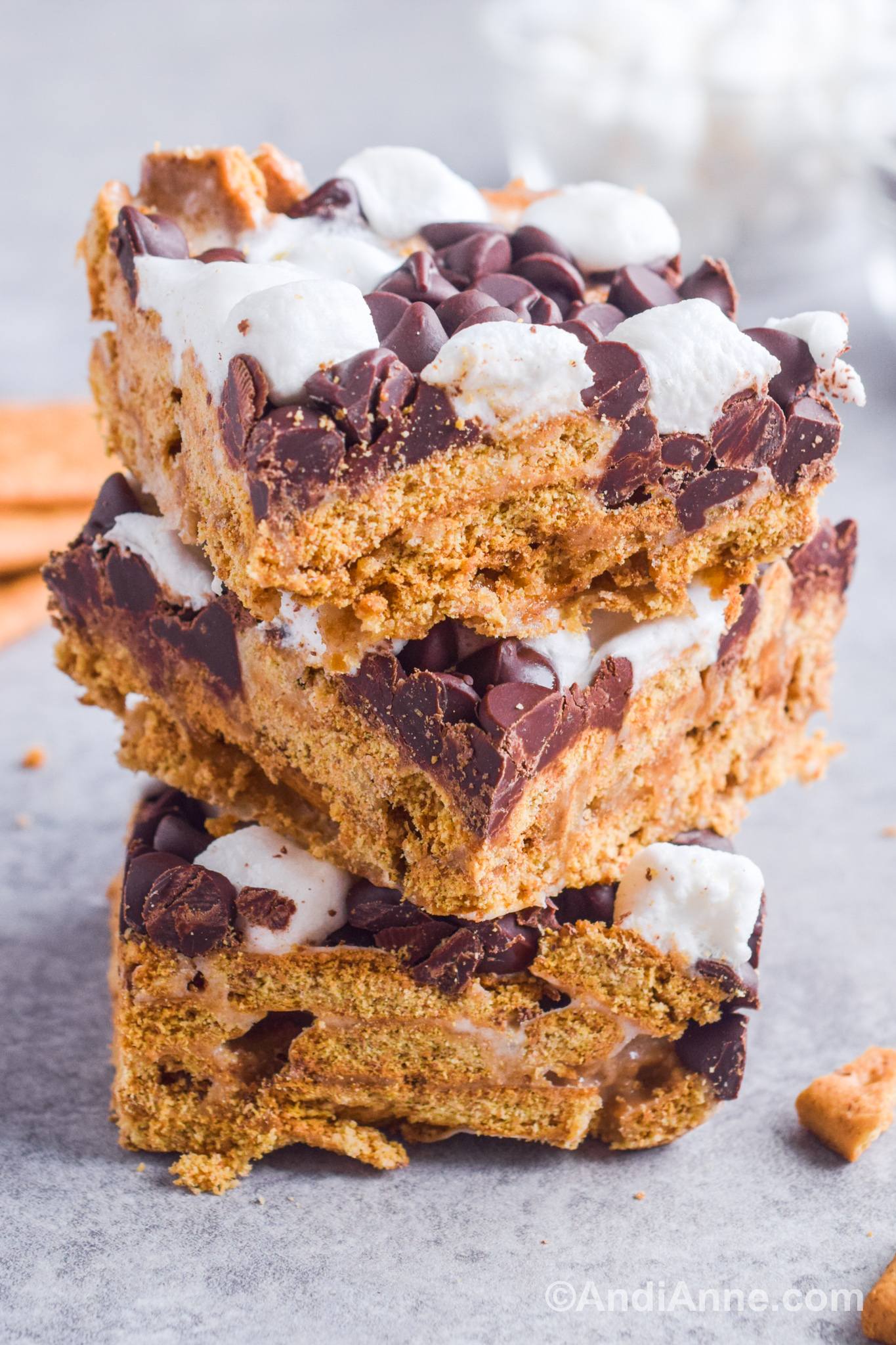 Three s'more bars stacked on top of eachother with a graham cracker base, chocolate chips and mini marshmallows on top.