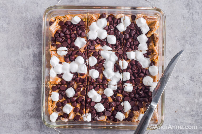 A square dish with smore bars inside sliced into squares and a sharp knife.