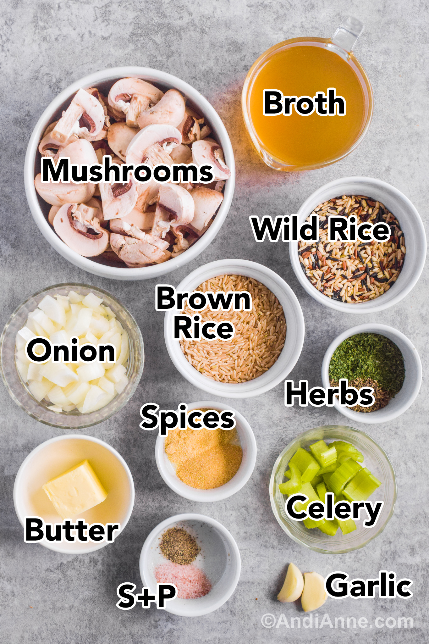 Ingredients in bowls on a counter including sliced mushrooms, wild rice, brown rice, chopped onion, herbs and spices, and celery.