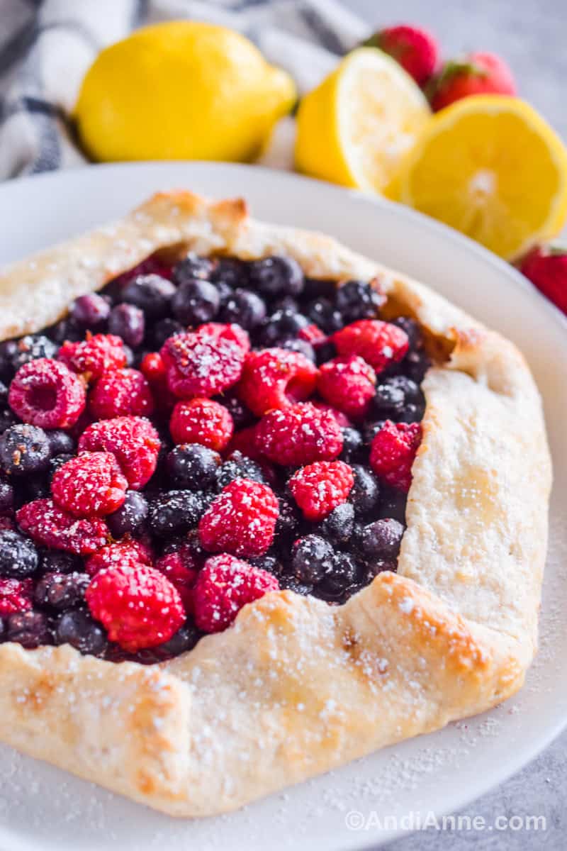 A side angle of the berry galette on a plate with lemons and strawberries in the background.