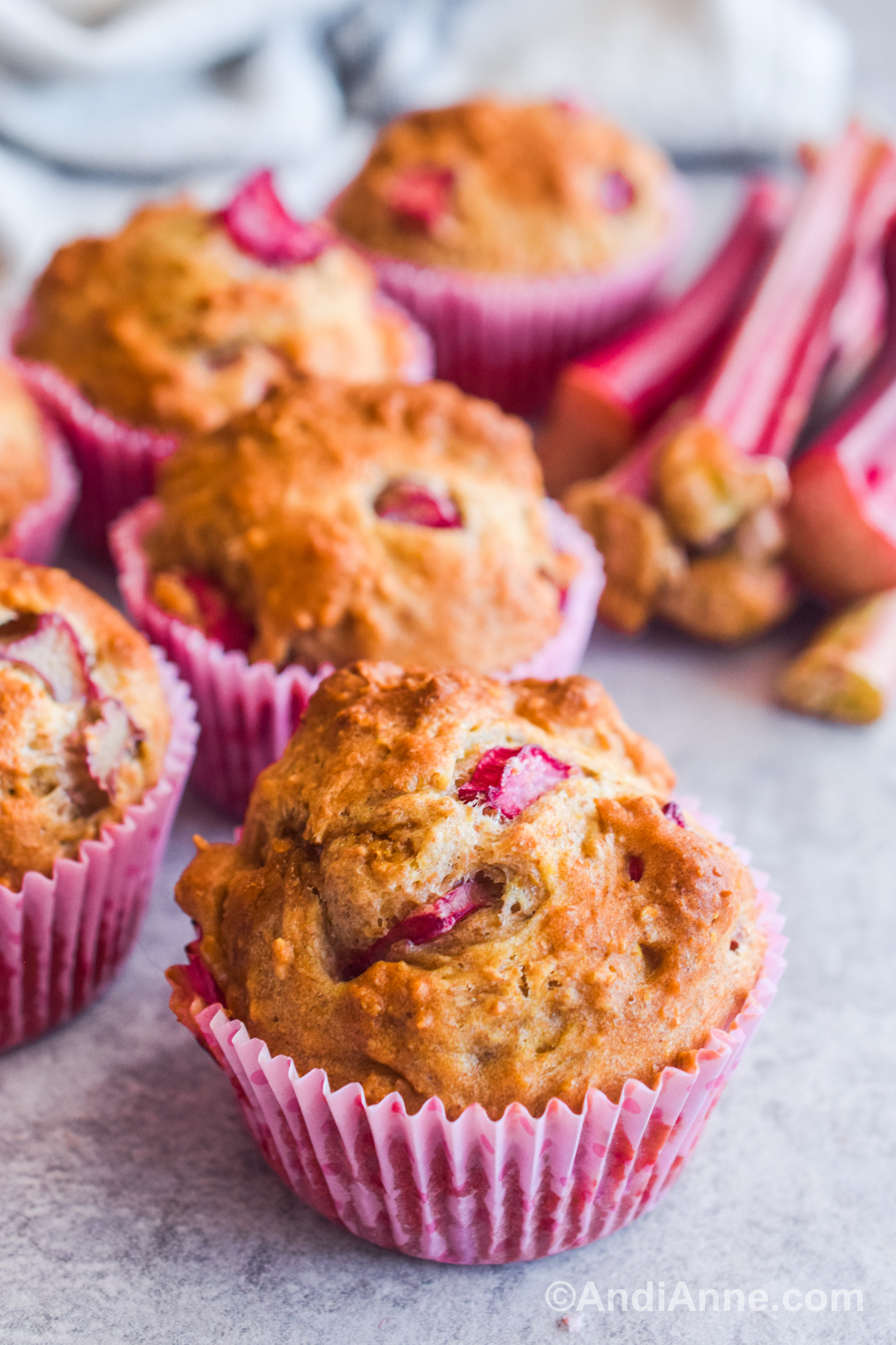 Close up of a few rhubarb muffins on a table with pink cupcake liners.