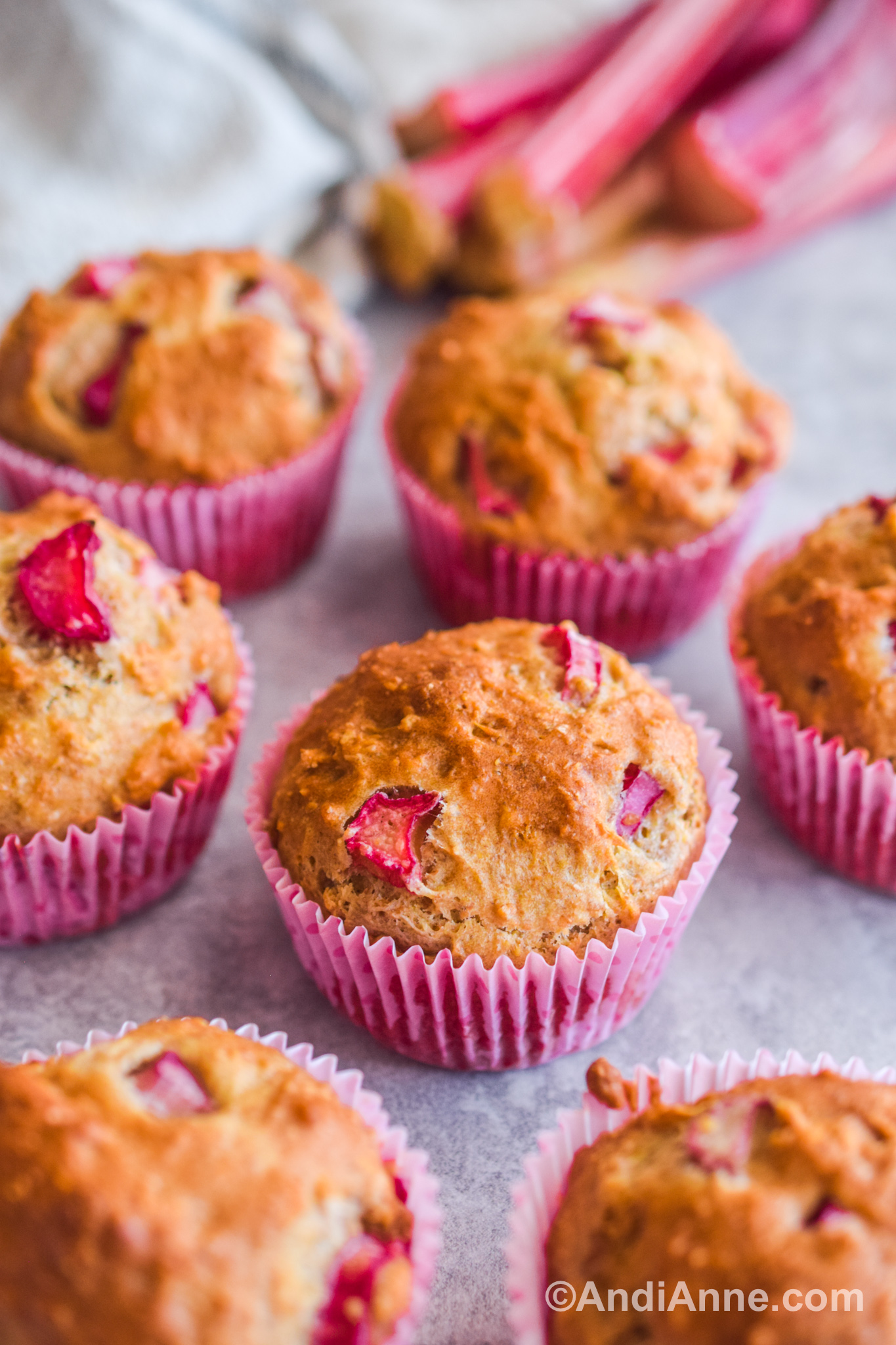 Rhubarb muffins close up with sticks of rhubarb in the background.