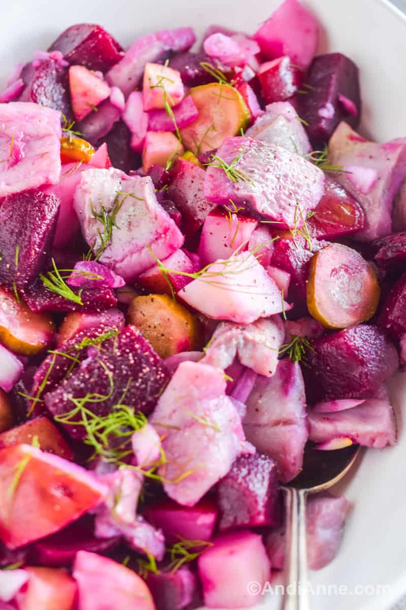 Close up of sillsallad with all ingredients having a pink hue from the pickled beets. Chopped fresh dill is sprinkled on top.