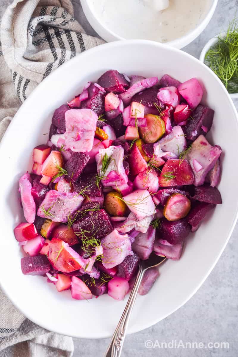 Herring beet potato salad in a white bowl with a spoon. Dill sprinkled on top.