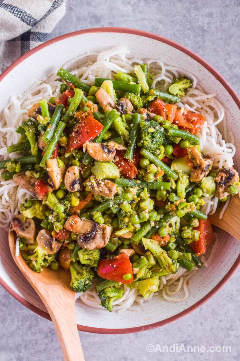 Looking down at the vegetable spaghetti recipe in a white serving bowl with two wood salad spoons.