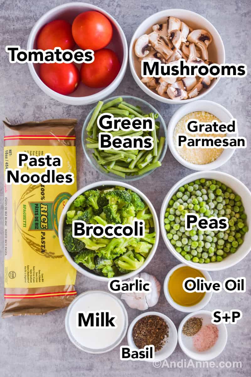 Recipe ingredients on the counter including a bowl of tomatoes, mushrooms, green beans, grated parmesan, broccoli, peas, rice noodles, milk, basil, olive oil, salt and pepper.
